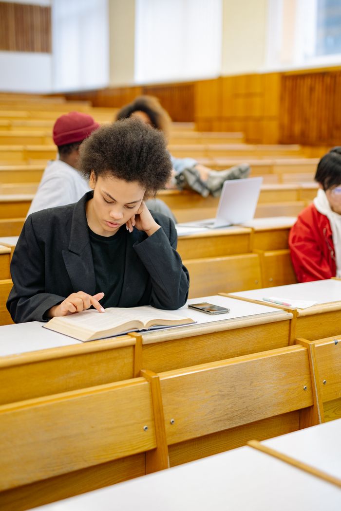 A young woman focuses intently on reading a book in a college lecture hall.