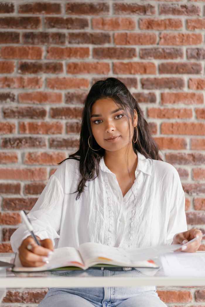 Young woman focused on studying with a book and notebook at her desk.